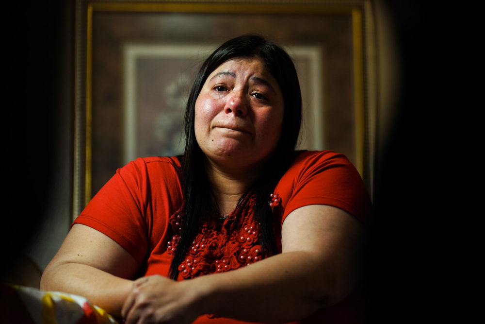Immigrant children families separated: Woman with long, drk hair and red top cries while sitting at table with hands folded.