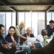Post-Pandemic Nonprofit: Group of 6 people in active discussion sit & stand around conference table