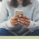 Texting teen health: young person in jeans and grey sweater sits holing phone texting