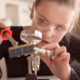 Virtual summer camps: Little girl with safety glasses works with a soldering iron on a computer component