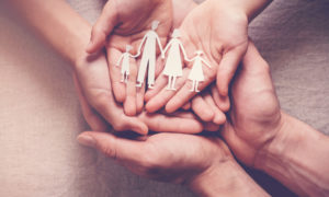 Therapeutic foster care, family unification: Hands palms up overlapping holding paper cutout of 2 adults with 2 children holding hands