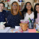 summer school: 3 young women and one lder woman stand together behind table of colorful craft supplis in front of more supplies on wall shelving and a "Welcome" sign