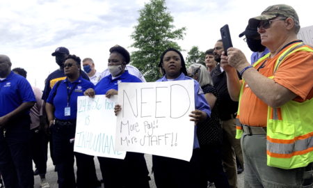 SC juvenile prison: Several workers in black pants and blue uniform shirts hold hand-printed signs and stand in protest of poor working conditions