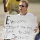 Alabama Medicaid expansion: Ray ables, man with blond hair and sunglasses holding wite sign with black marker text "Everyone should have the right to see a doctor."