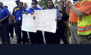 SC juvenile protest: Several workers in black pants and blue uniform shirts hold hand-printed signs and stand in protest of poor working conditions