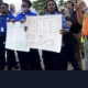 SC juvenile protest: Several workers in black pants and blue uniform shirts hold hand-printed signs and stand in protest of poor working conditions