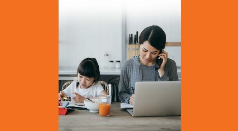 2021 KIDS COUNT Data Book: Asian mother working at kitchen table on laptop with daughter doing homework and eating beside her