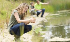 high school stem projects, environmental career development grants: high school girl looking at water quality sample next to body of water