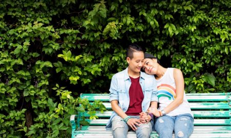Northwest LGBTQ+ and black community COVID recovery grants: LGBTQ+ couple on park bench with bushes behind them
