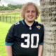 Mental health Kids Isolation Reentry: Young man with blonde, curly hair wearing black #30 football jersey leans against palm tree trunk in green grassy field