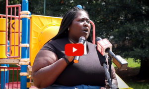 child tax credit: Black woman with long braids and brown shirt holding microphone speaks to outdoor crowd