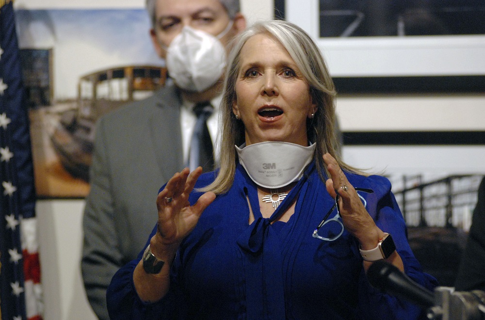 New Mexico distributing 1.8 million in pandemic aid to former foster youth: Woman with long gray hear in blue business suits stands at microphone speaking at event