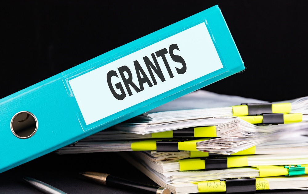 seeking grants with limited time and resources: graphic of stack of paper and binder with word "grants"