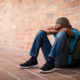 Black children investigated by CPS: sad black child sitting against brick wall with head in arms