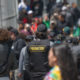 Juvenile diversion: Person wearing black baseball cap and black vest with patch reading PROBATION in yellow letters on backrowd of people walking on sidewalk