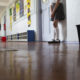 Student punishment: young girl leans against wall alone in school hallway