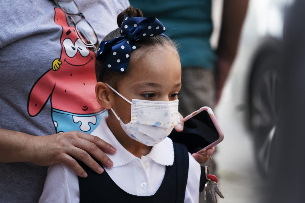 delta variant afterschool: young Elementary-age Black girl with black hair in top bun with large navy bow wearing dark navy and white top and face mask