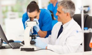STEM apprenticeship and career pathway training grants: senior researcher helping pupil as she looks through microscope