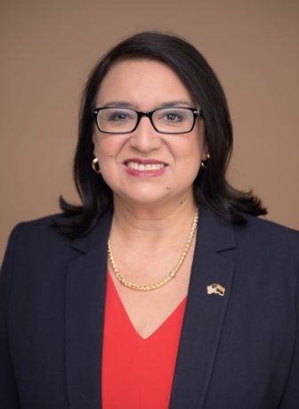 Youth justice and legal aid: January Contreras headshot of smiling dark-haired woman with black-framed glasses wearing navy suit with red blouse and gold necklace