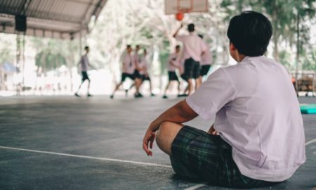 LGBTQ youth sports participation brief: sad youth watching other play basketball