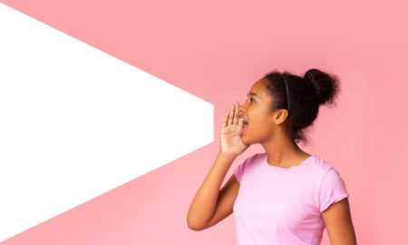 Teach civil discourse: Black pre-teen girl with blacj hair in bun in pink top holds handnear mouth shouting with white cutout on dark pink background forming shape of megaphone