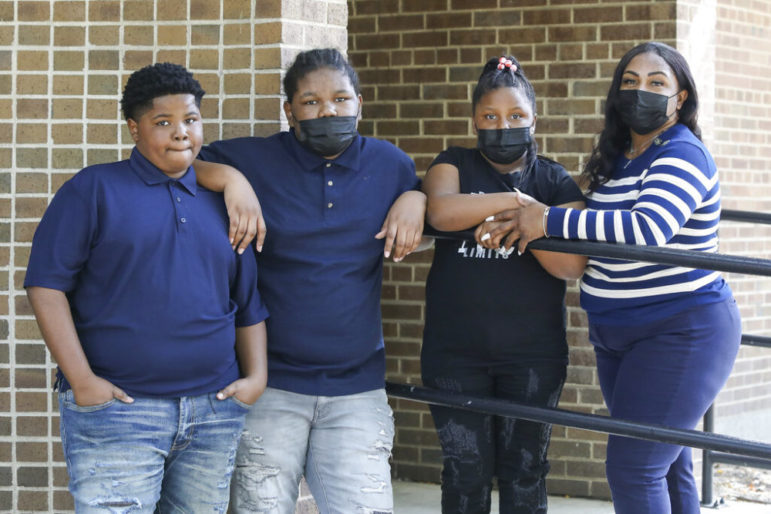 Police use excessive force with children: Black family of four - 2 teen sons, 1 teen daughter and mother - stand with arms linked in front of red brick building