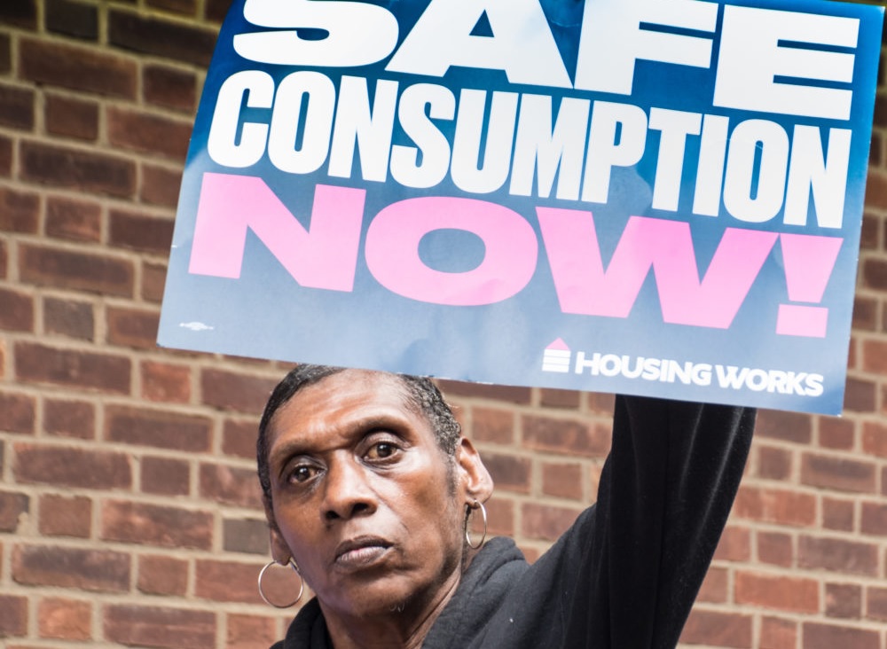 medical treatments for substance use for New York jails: protester holding "safe consumption now" sign