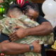 YMCA Urban Warriors: Black man with braids facing camera hugging man with short brown hair wearing camo military fatigues standing in front of a decorated Christmas tree