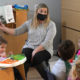 pandemic child care crisis hampers economy: woman reading to small children with mask on