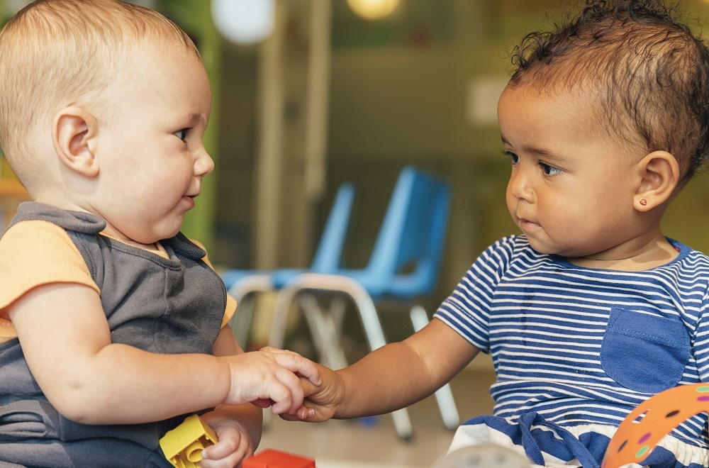 Kids' share report on federal expenditures: small white boy and small black boy playing with building blocks together touching hands