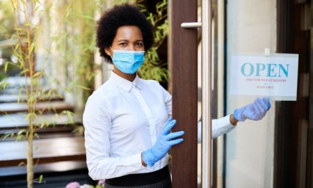 minority-led business support grants: Black woman with mask putting up open sign on door