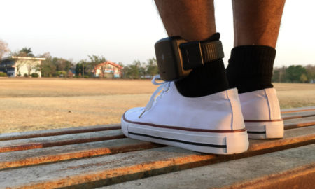 Juvenile diversion and probation: Closeup of two feet wearing white tennis shoes and black socks with an ankle monitor on left ankle
