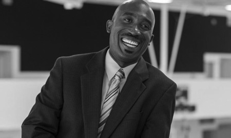 Daniel Shoy Jr newsmaker headshot: smiling bald black man in suit and tie