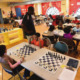 BOOST: Several young students sit at tables in colorful classroom playing chess