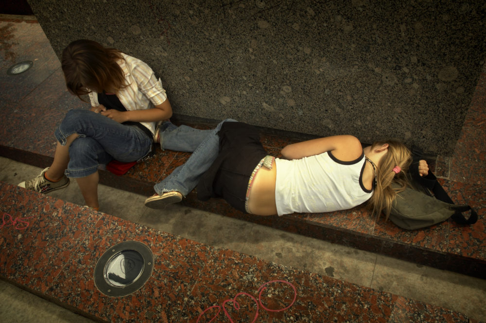 NY Homeless paymaents:Two peple on a cement wall, one blonde sleeping and one brunette sitting crouched over