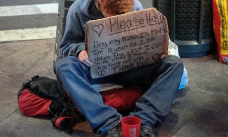 New York homeless payments: A homeless male sits on a New York City sidewalk holdwith head hanging hidden behind large cardboard sign with a message asking for help.