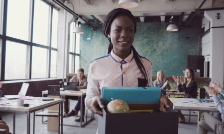 youth employment grants: young black woman walking into new job with box of things for desk