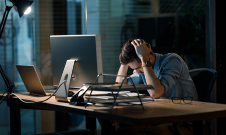 nonprofits misclassify workers: frustrated man with hands on head at computer in dark room