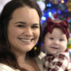 Abortion and Adoption: Close-up of smiling young dark-haired woman holding infant in red plaid top with large red bow headband.