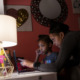 Digital divide virus: Older Black woman leans over shoulder of young black girl sitting at desk looking at laptop screen