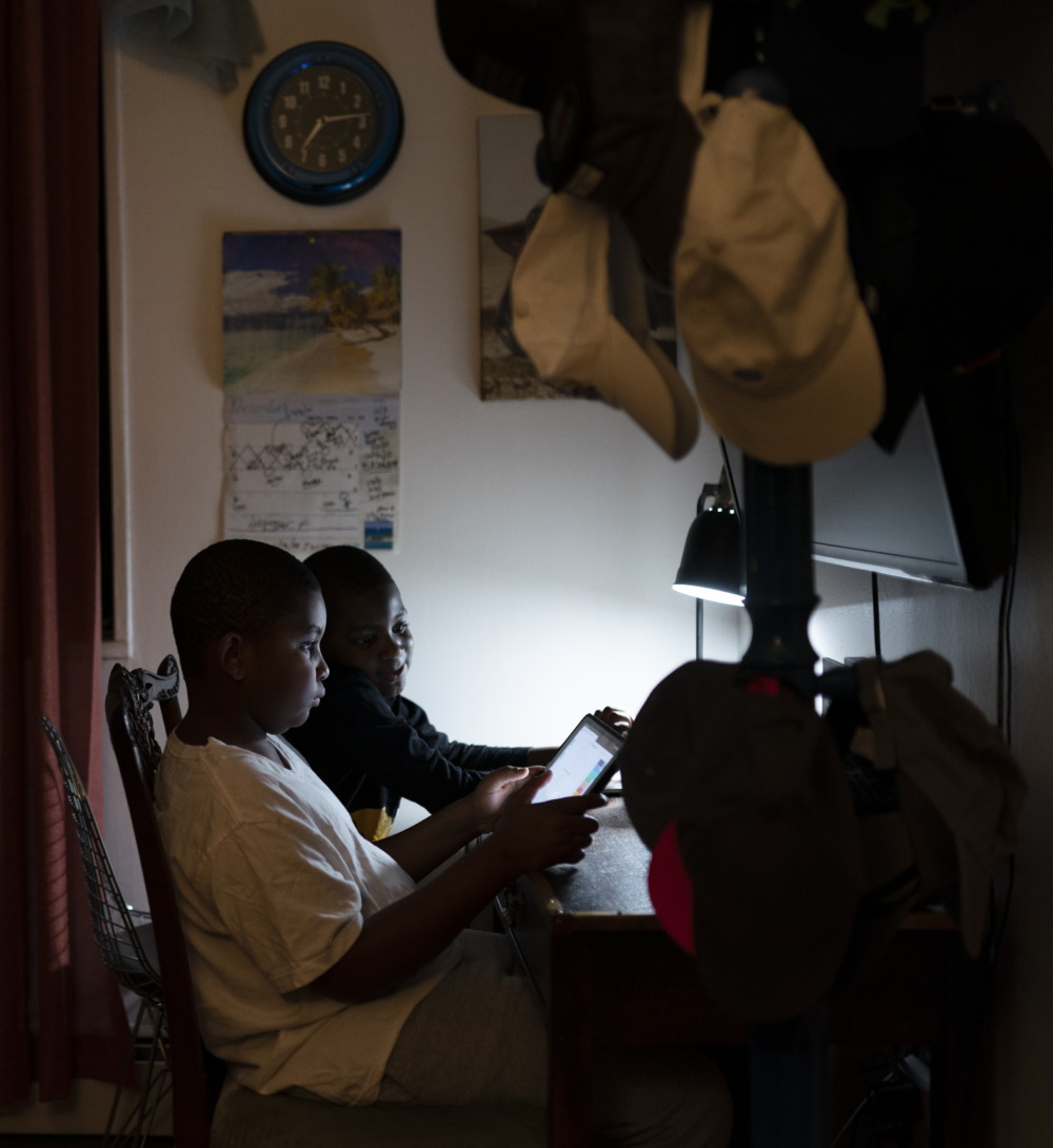 Digital divide virus: Two young Black boys sit at desk looking at laptop they are sharing