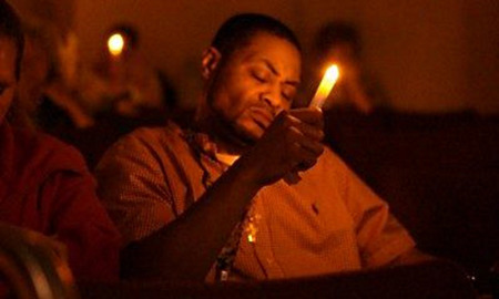 Accidental drug overdose: Black man wearing tan shirt sits holding lit candle in dark room