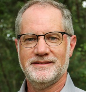 Marc Schindler headshot middle-aged, grey-haired man with gbeard wearing dark-framed glasses.