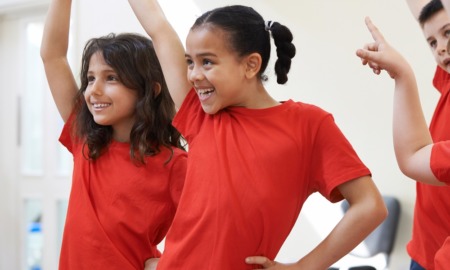 youth theatre grants: two young girls of color in red shirts practice theatre dancing