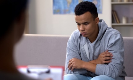 community youth violence prevention research grants: sad and troubled teen in grey hoodie talking to therapist