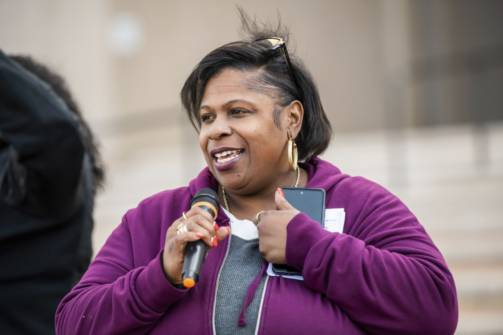 Tamir Rice: Black woman with black hair pulled back wearing purple sweatshirt and gray shirt speaks into hand-held microphone.