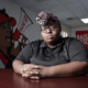 Unions: Young black woman with black glasses and red print head warp in black top sits at office desk