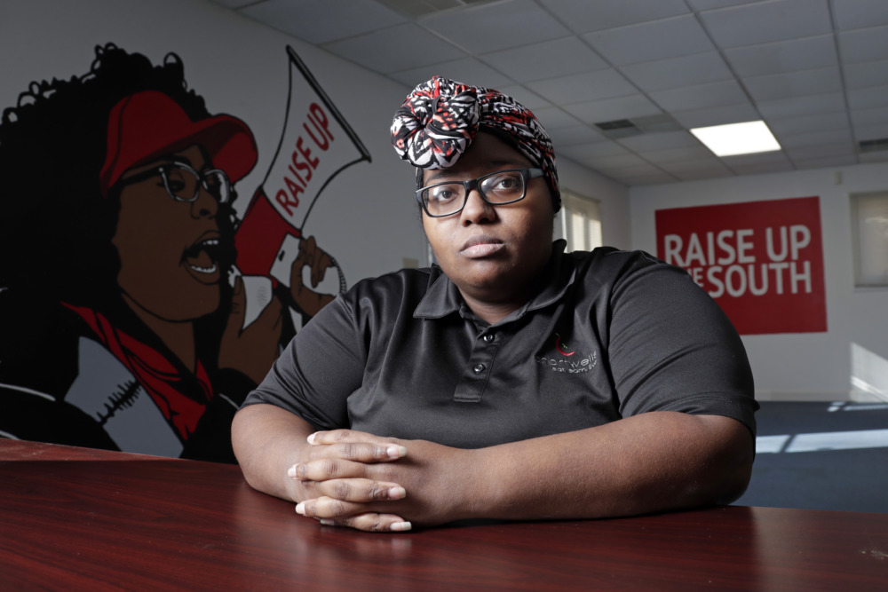 Unions: Young black woman with black glasses and red print head warp in black top sits at office desk