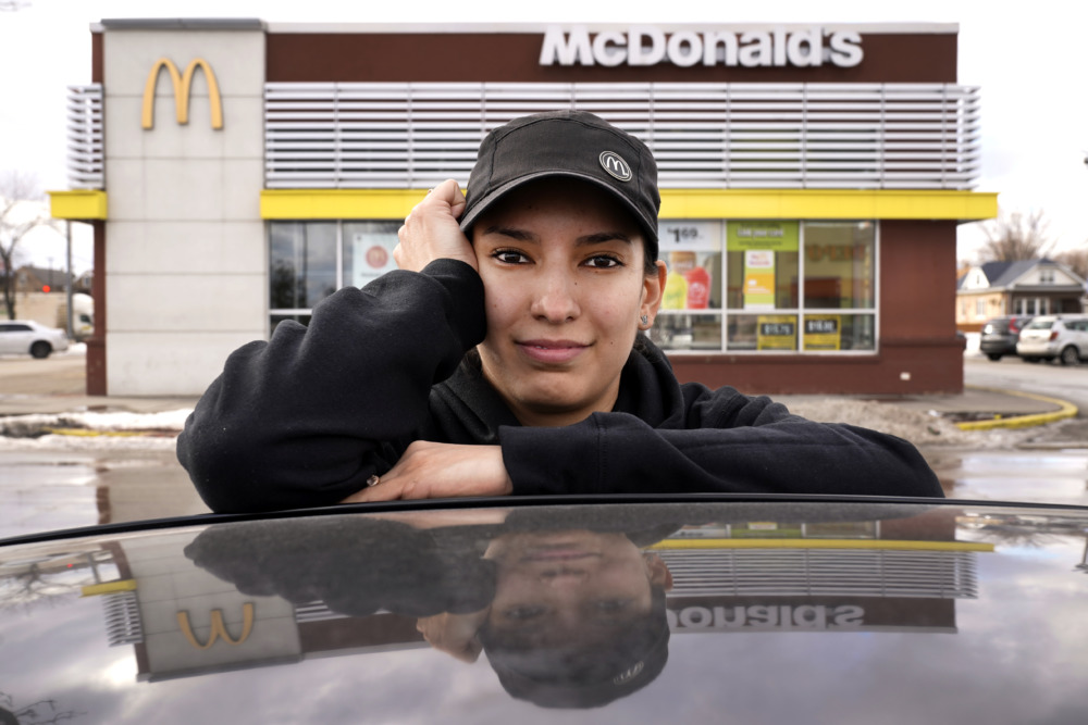 Unions: Young white woman in black top and baseball cap stands n front of McDonalds building