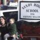 Sandy Hook: Woman childing toddler stand s amidst cars next to sign saying " Sandy Hook Elementary School"